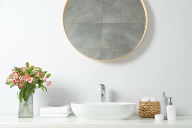 Vase with beautiful Alstroemeria flowers and toiletries near sink in bathroom