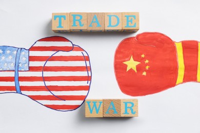 Photo of Wooden cubes with words Trade War, boxing gloves with American and Chinese flags drawn on white paper, top view