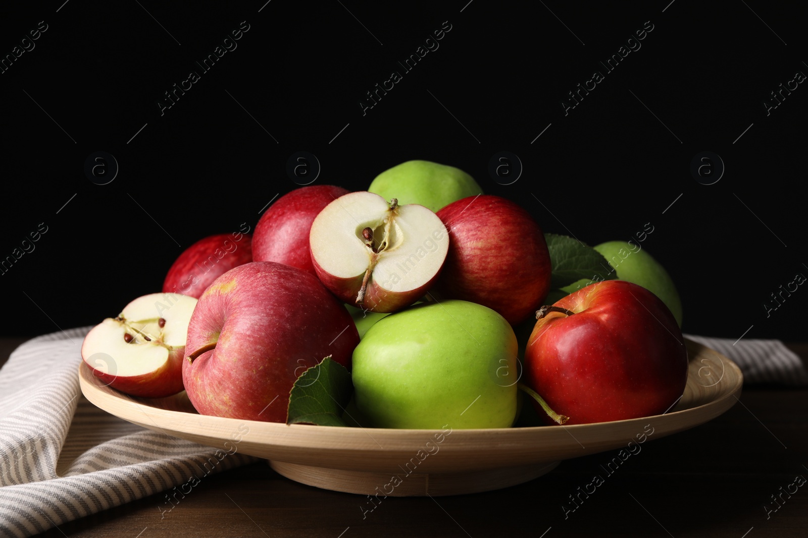 Photo of Plate with fresh ripe apples and leaves on wooden table against dark background