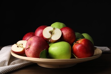 Plate with fresh ripe apples and leaves on wooden table against dark background