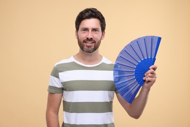 Photo of Happy man holding hand fan on beige background