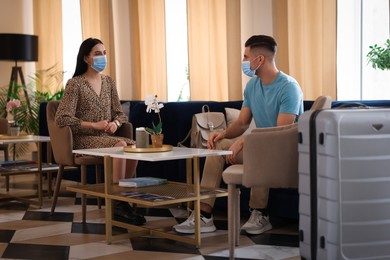 Photo of Couple with medical face masks having conversation while waiting in hotel hall