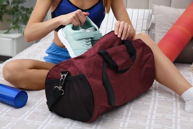 Photo of Woman packing sports stuff for training into bag at home, closeup