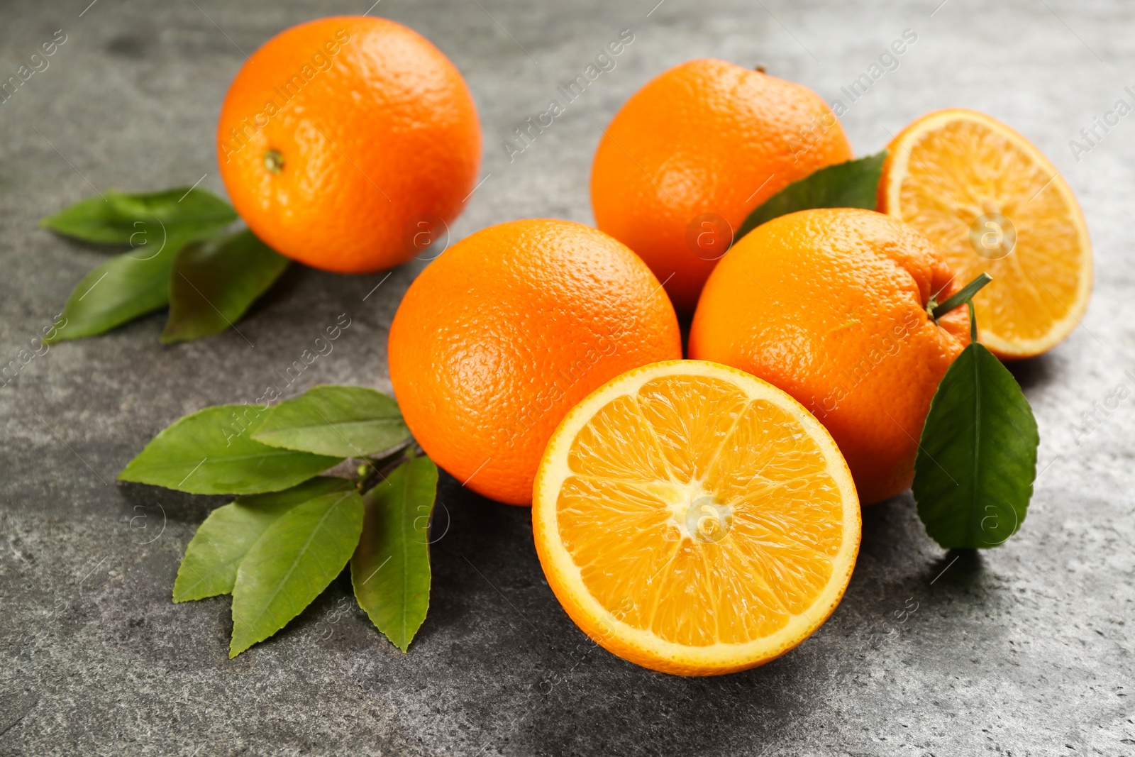 Photo of Whole and cut delicious ripe oranges on grey table