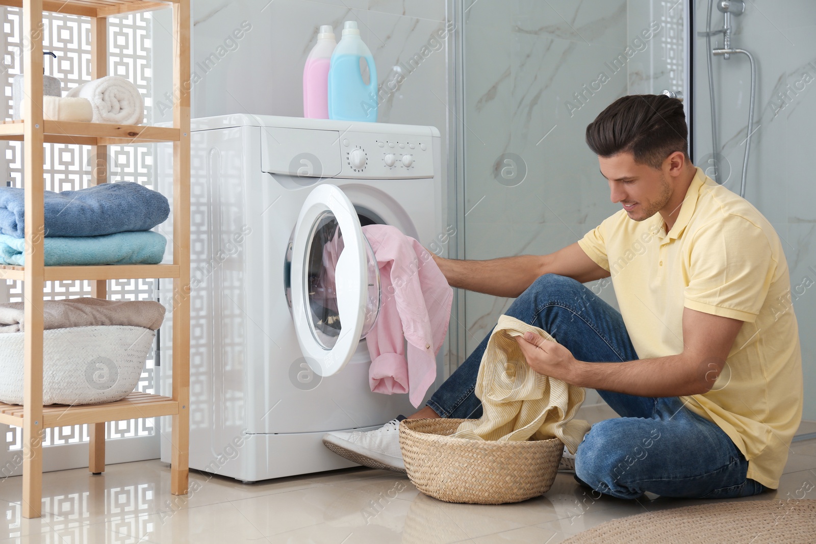 Photo of Man putting clothes into washing machine in bathroom. Laundry day