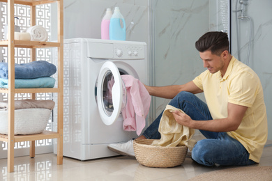 Man putting clothes into washing machine in bathroom. Laundry day