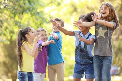 Cute little children playing with soap bubbles outdoors on sunny day