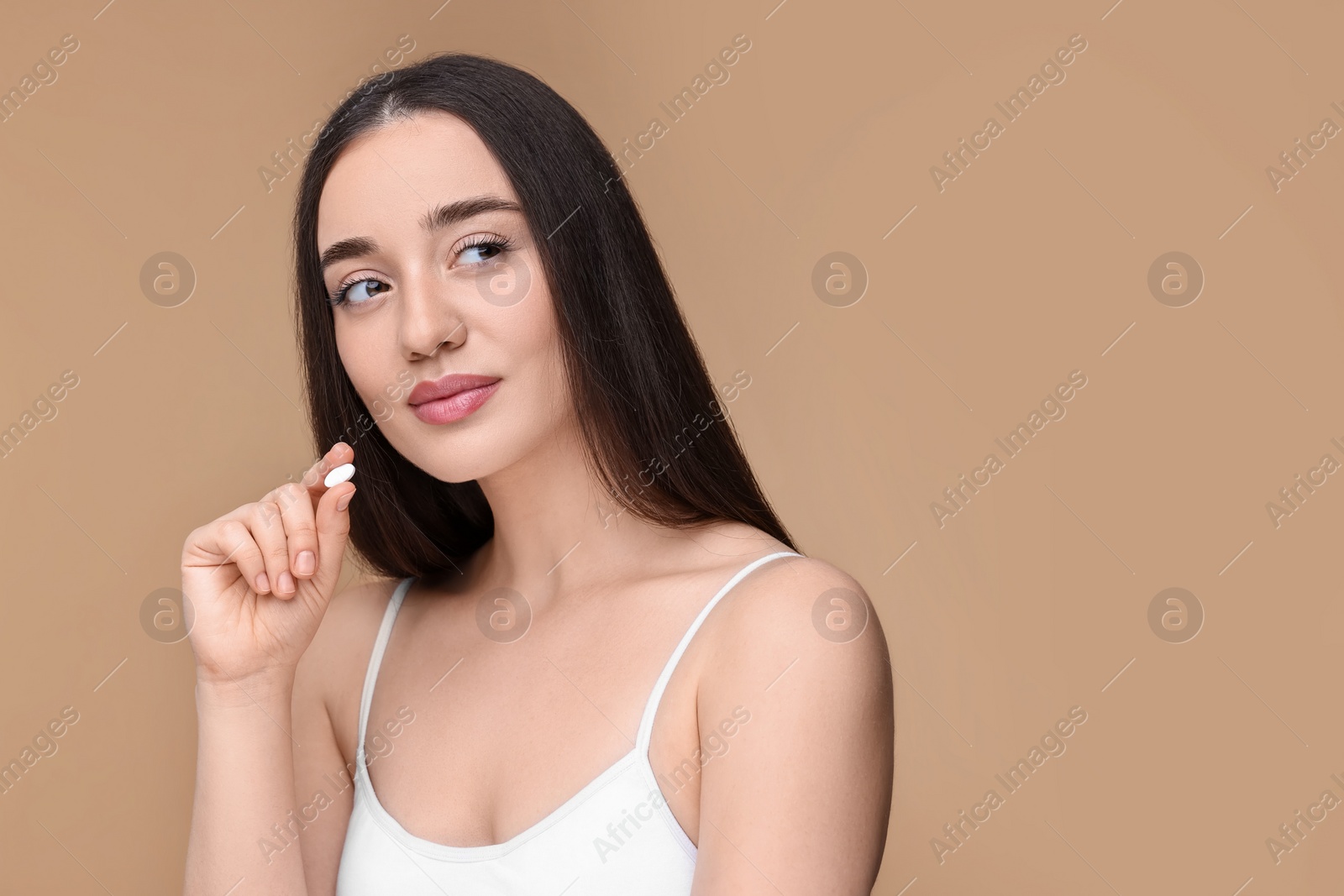 Photo of Beautiful young woman with vitamin pill on beige background. Space for text