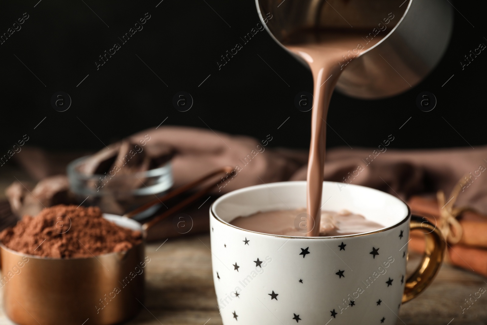 Photo of Pouring hot cocoa drink into cup on wooden table