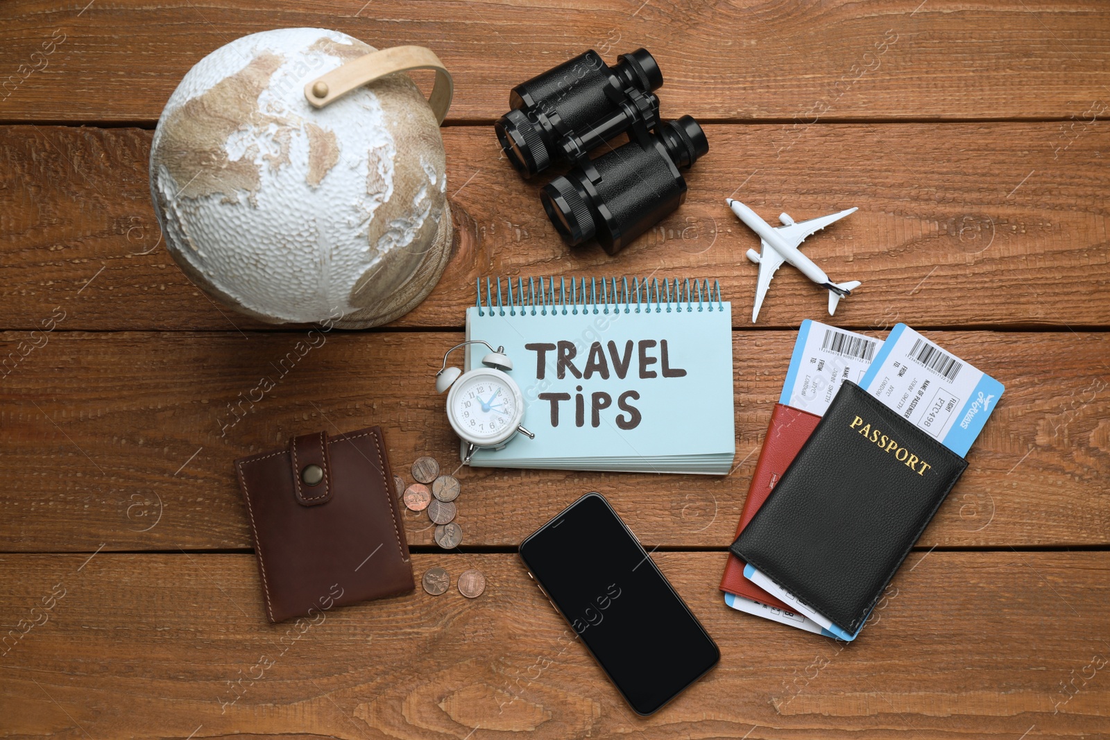 Photo of Notebook with phrase Travel Tips, smartphone and tourist items on wooden table, flat lay