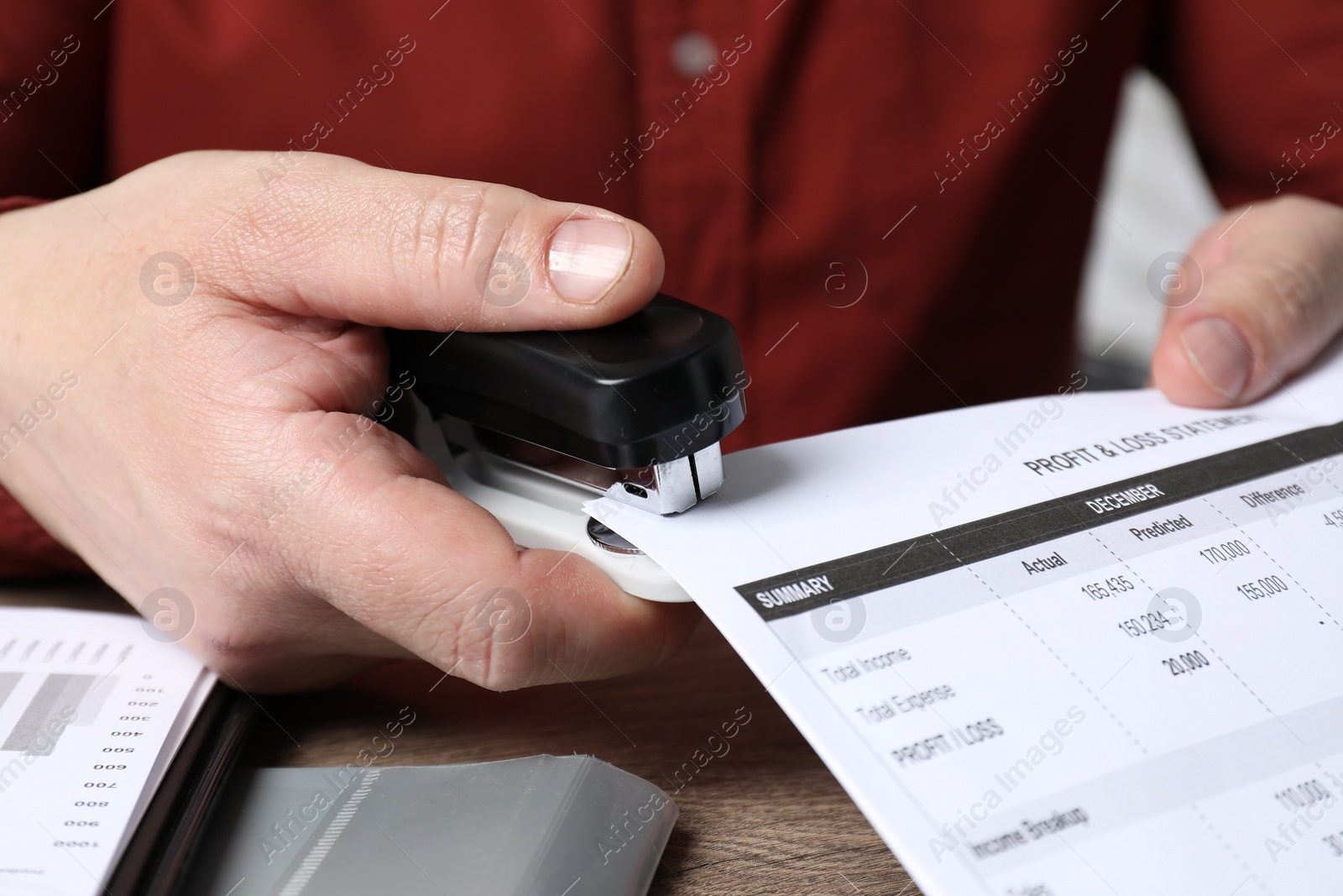 Photo of Man with documents using stapler at wooden table, closeup