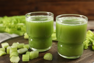 Photo of Glasses of delicious celery juice and vegetables on wooden board, closeup