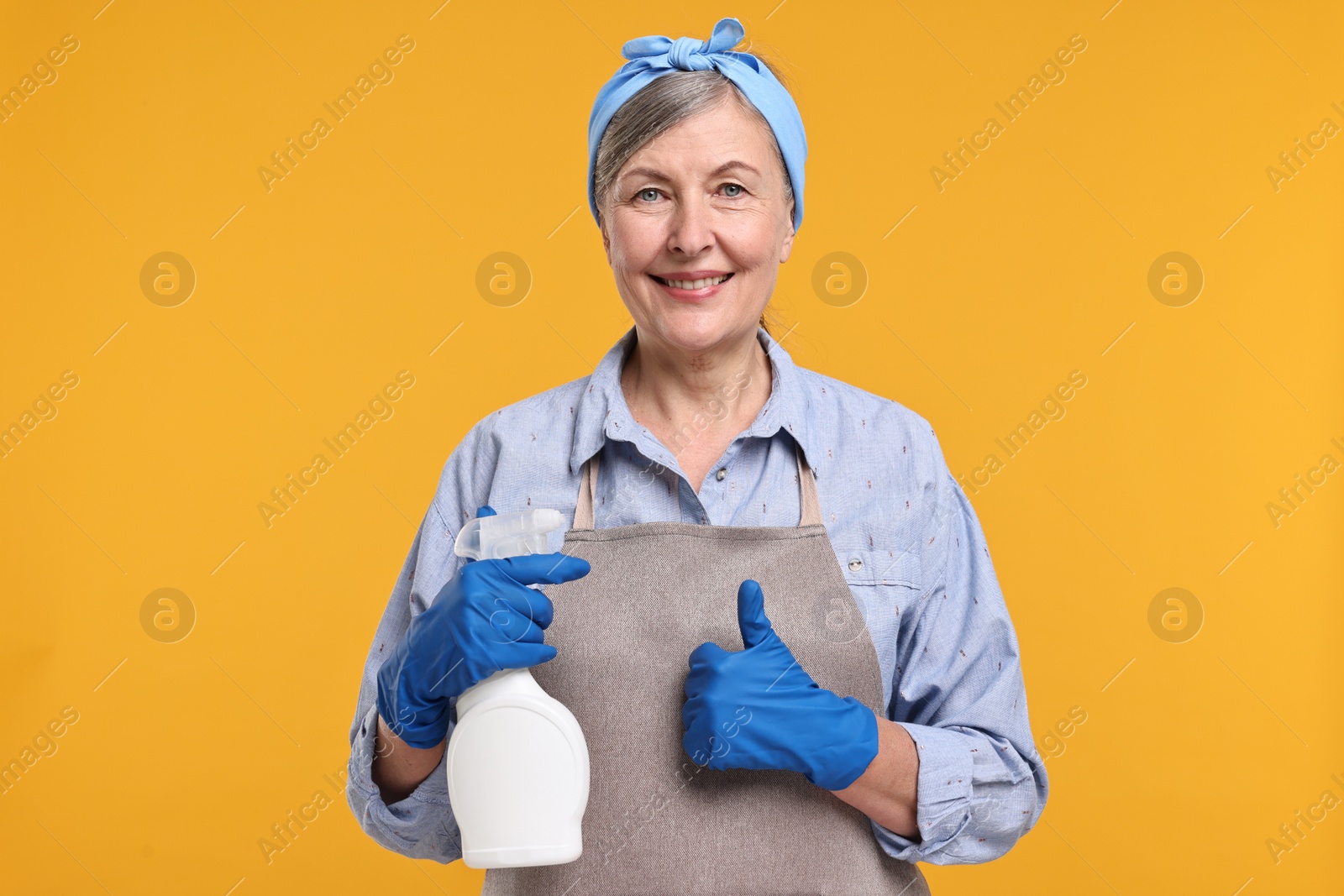 Photo of Happy housewife with spray bottle showing thumbs up on orange background
