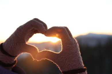 Woman making heart with her hands in mountains at sunset, closeup. Winter vacation