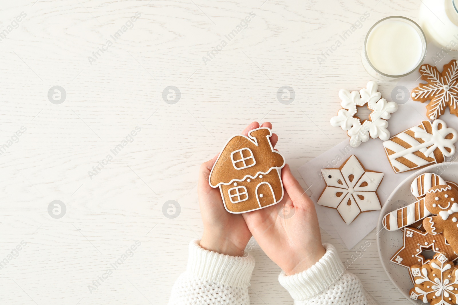 Photo of Woman holding delicious homemade Christmas cookie at white table, top view. Space for text