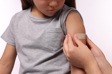 Woman sticking plaster on girl's arm after vaccination against white background, closeup