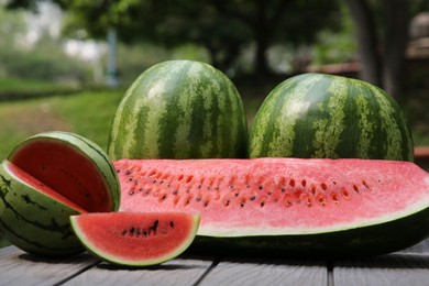 Photo of Different ripe whole and cut watermelons on wooden table outdoors