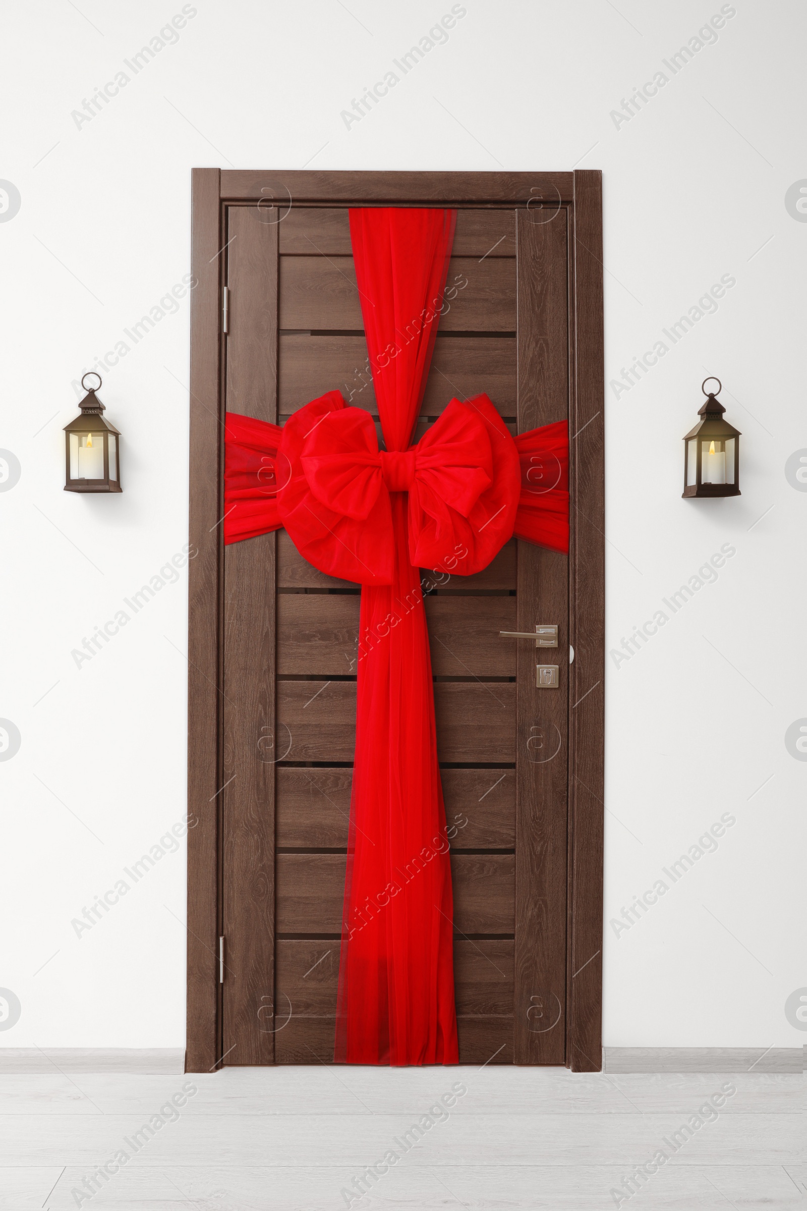 Photo of Wooden door with beautiful red bow and lanterns hanging on wall. Christmas decoration