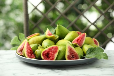 Cut and whole green figs on white marble table against blurred background, closeup. Space for text