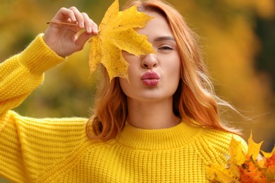 Photo of Beautiful woman covering eye with autumn leaf outdoors