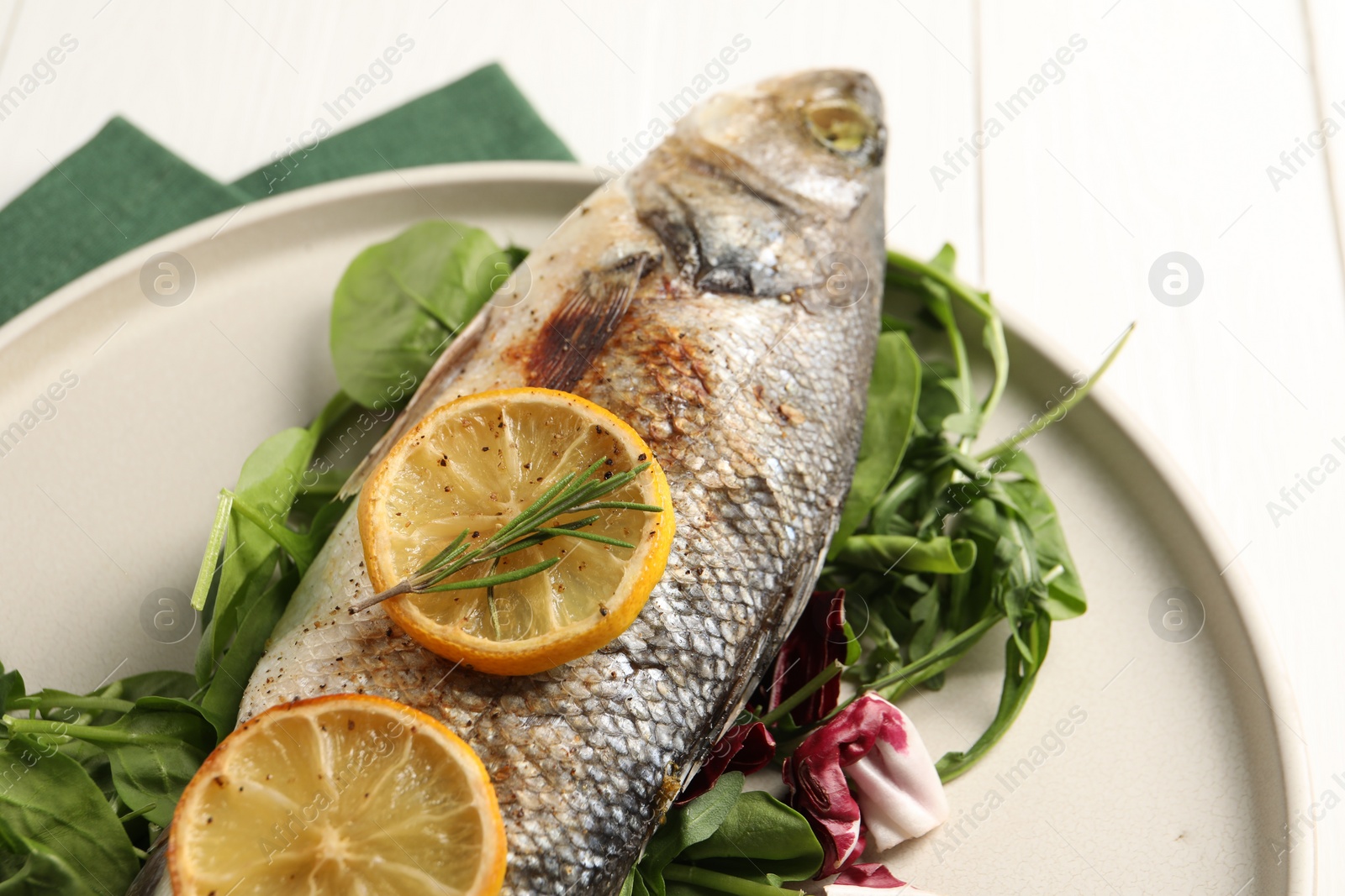 Photo of Baked fish with spinach and lemon on white wooden table, closeup