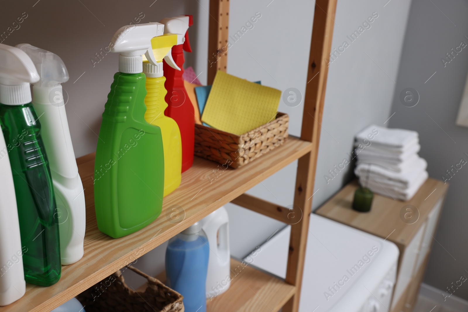 Photo of Different detergents and rags on wooden rack in laundry room