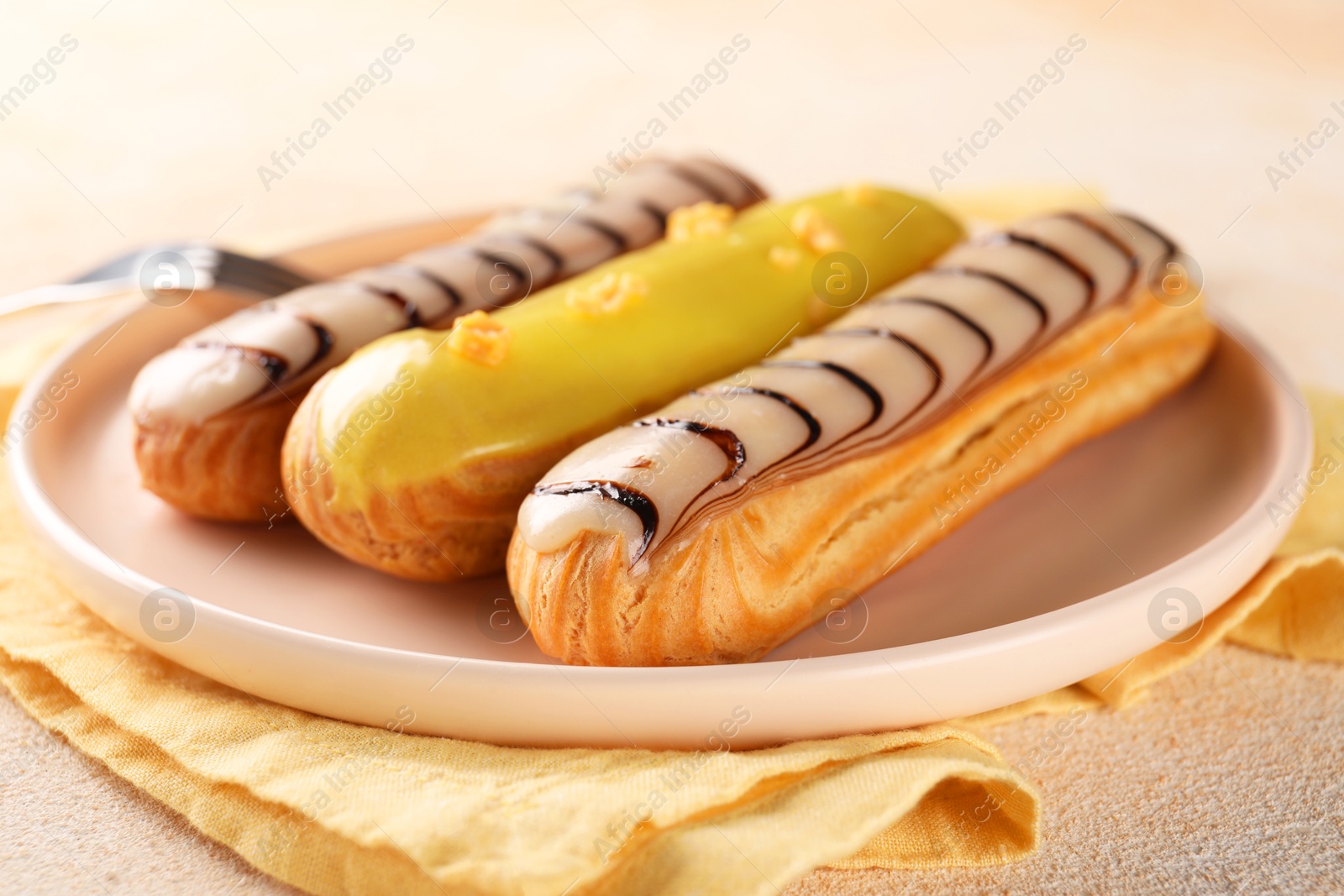 Photo of Different tasty glazed eclairs served on color textured table, closeup