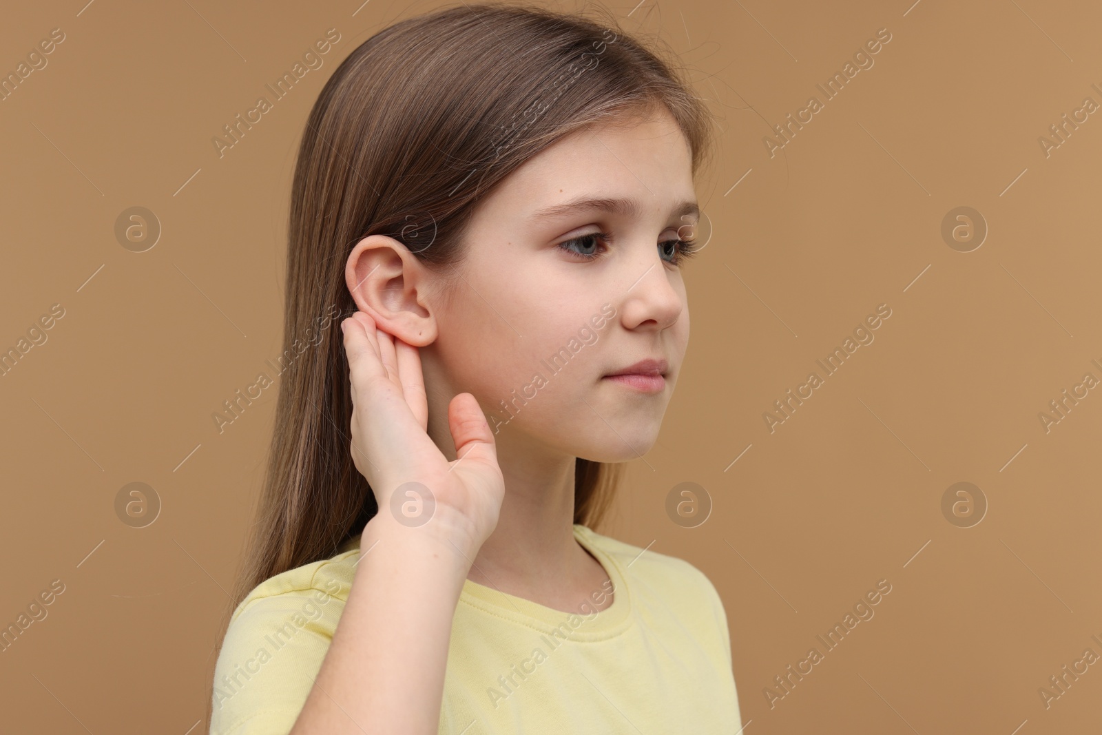 Photo of Little girl with hearing problem on pale brown background, space for text