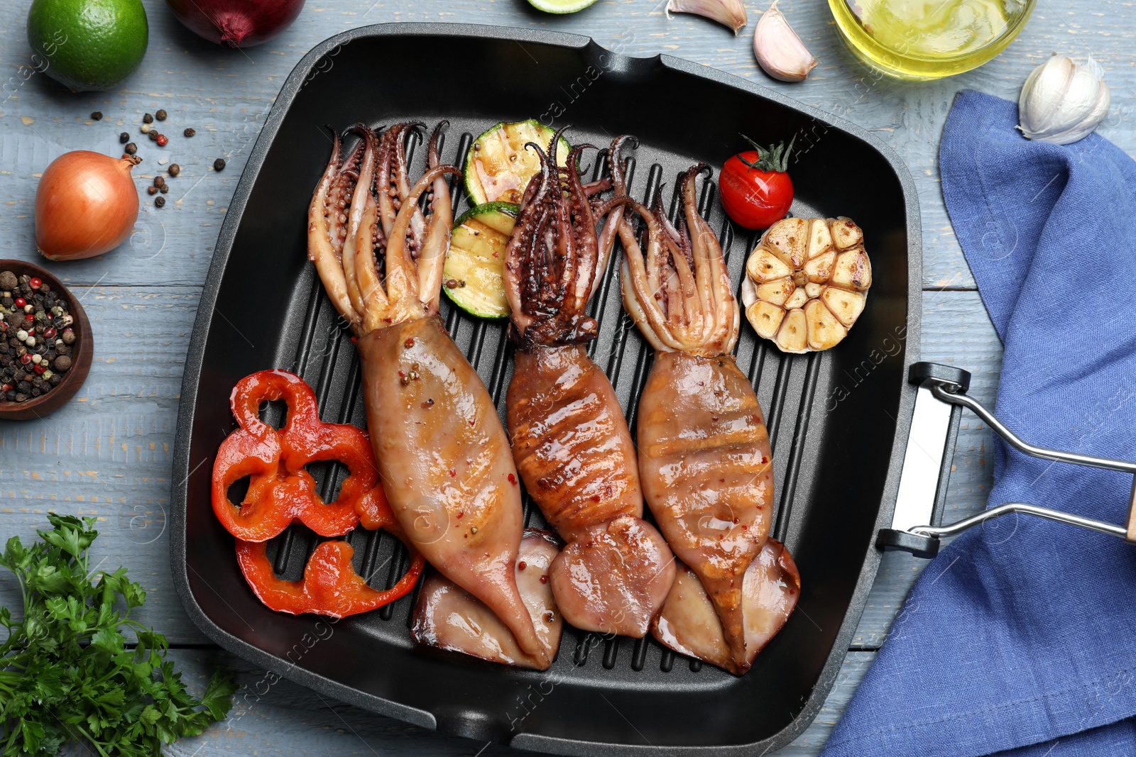 Photo of Tasty grilled squids with vegetables served on grey wooden table, flat lay