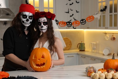 Photo of Couple in scary bride and pirate costumes with carved pumpkin indoors, space for text. Halloween celebration