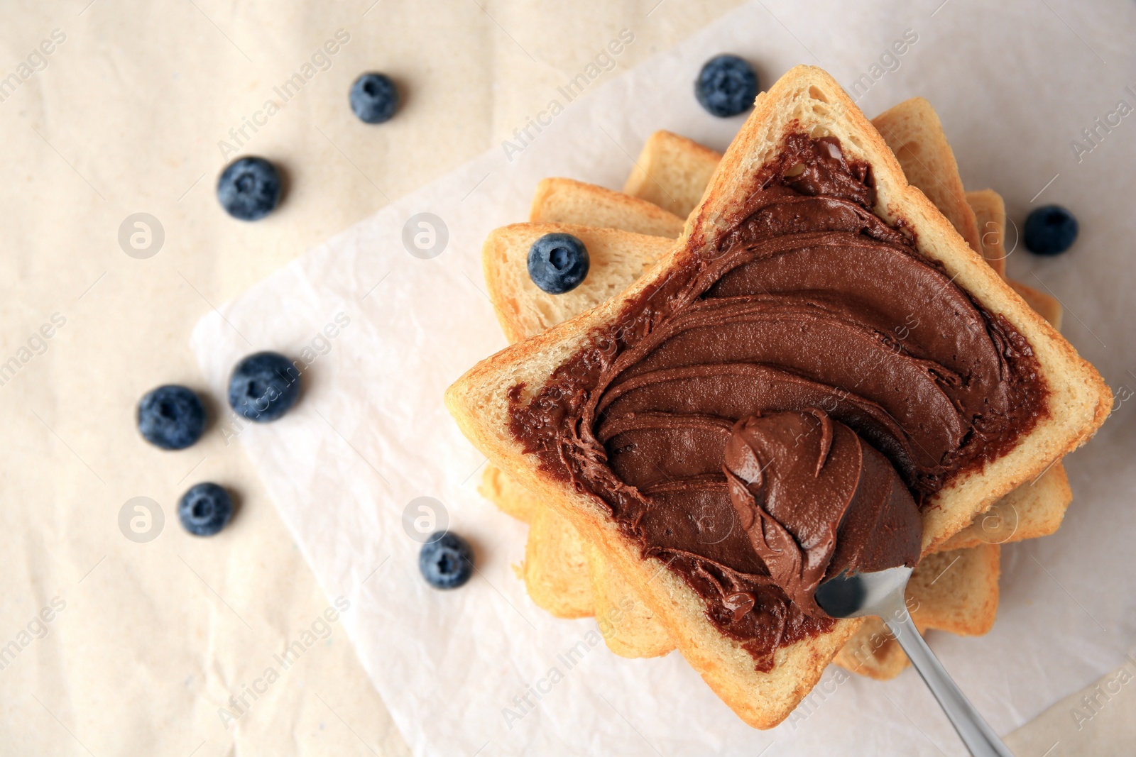 Photo of Tasty toast with chocolate paste and blueberries on parchment paper, flat lay