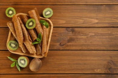 Photo of Delicious fruit leather rolls and kiwis on wooden table, flat lay. Space for text