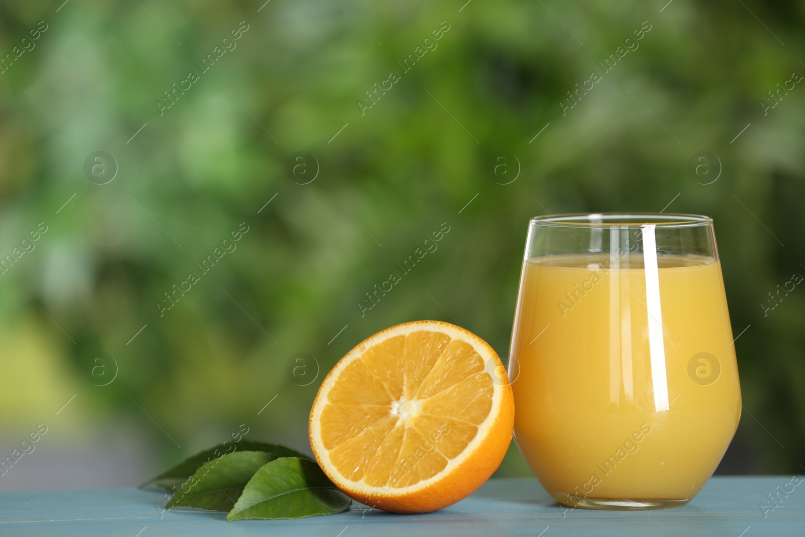 Photo of Delicious orange juice and fresh fruit on light blue wooden table against blurred background. Space for text