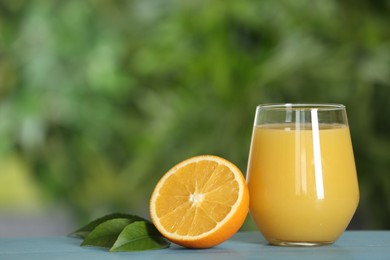 Photo of Delicious orange juice and fresh fruit on light blue wooden table against blurred background. Space for text