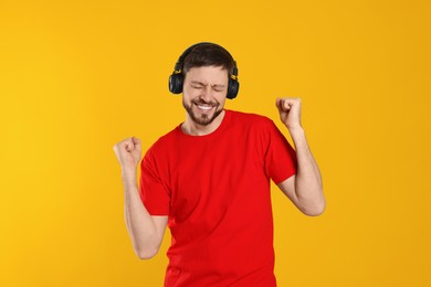 Happy man in headphones enjoying music and dancing on orange background