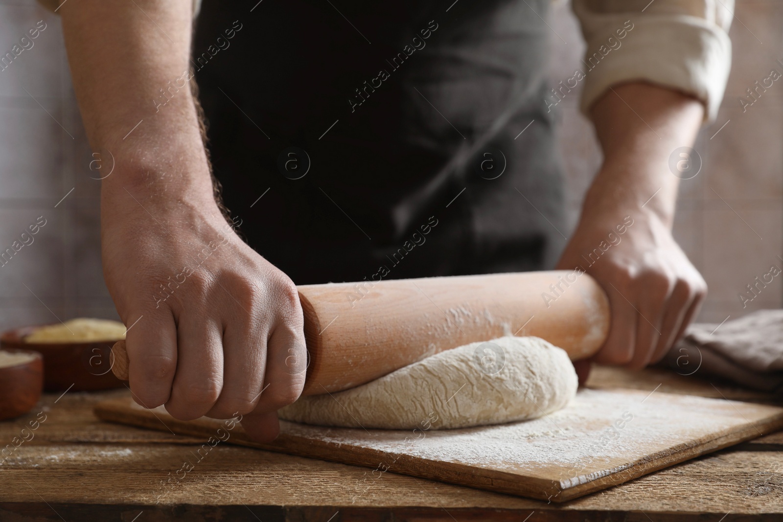 Photo of Man rolling raw dough at wooden table, closeup