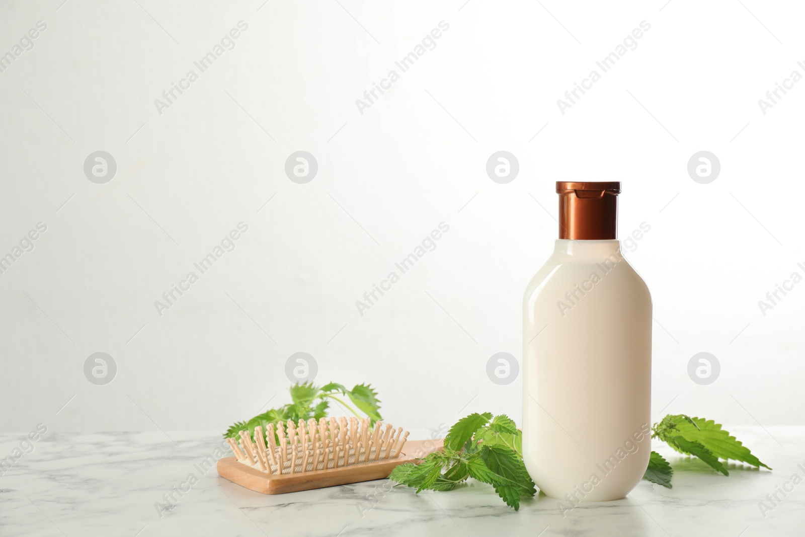 Photo of Stinging nettle, cosmetic product and brush on white marble background, space for text. Natural hair care