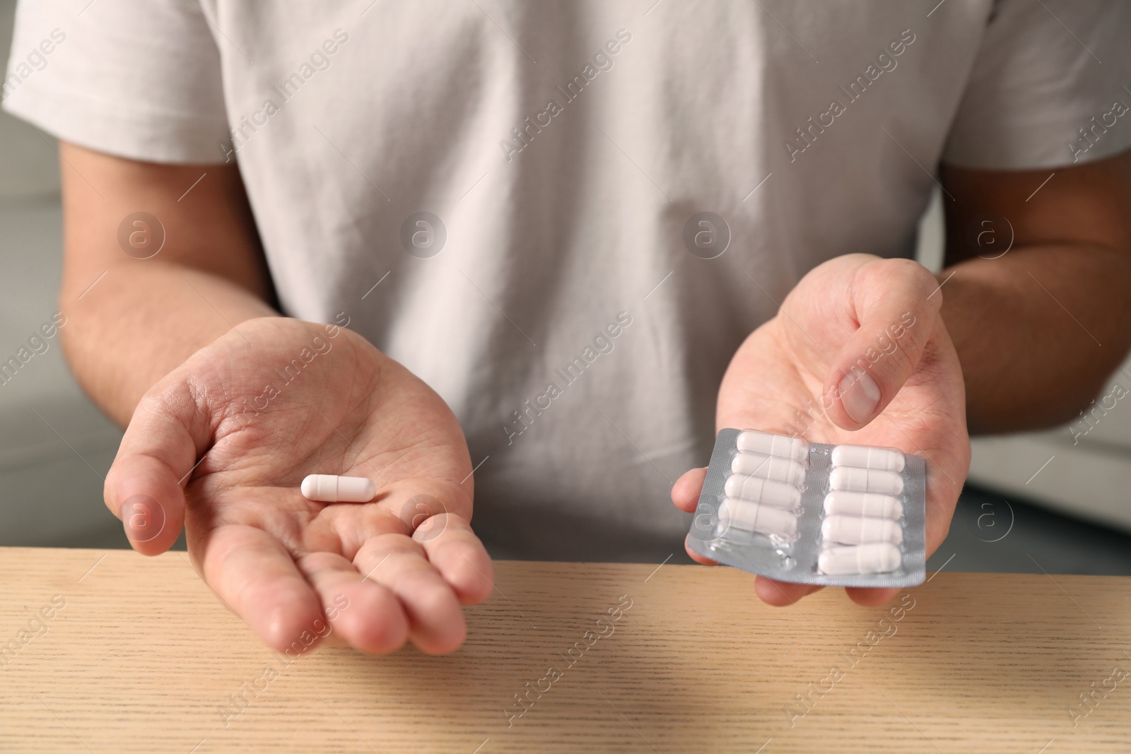 Photo of Man holding pills at wooden table, closeup