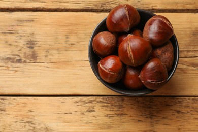 Photo of Fresh edible sweet chestnuts in bowl on wooden table, top view. Space for text