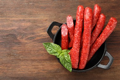 Photo of Thin dry smoked sausages and basil on wooden table, top view. Space for text