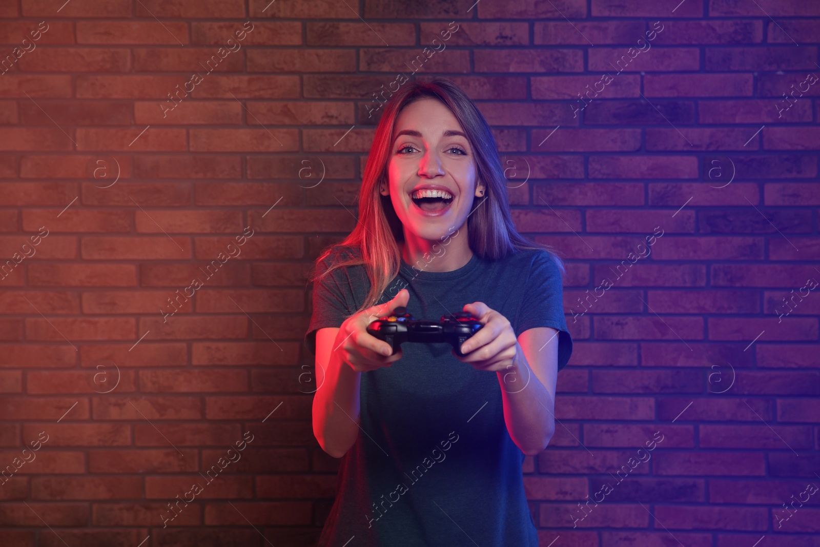 Photo of Emotional young woman playing video games with controller near brick wall