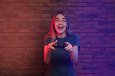 Photo of Emotional young woman playing video games with controller near brick wall