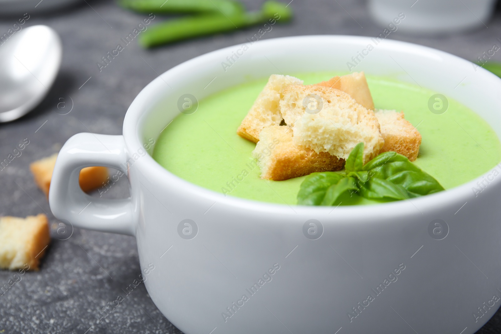 Photo of Green pea soup with croutons in bowl on table