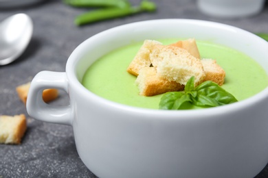 Photo of Green pea soup with croutons in bowl on table