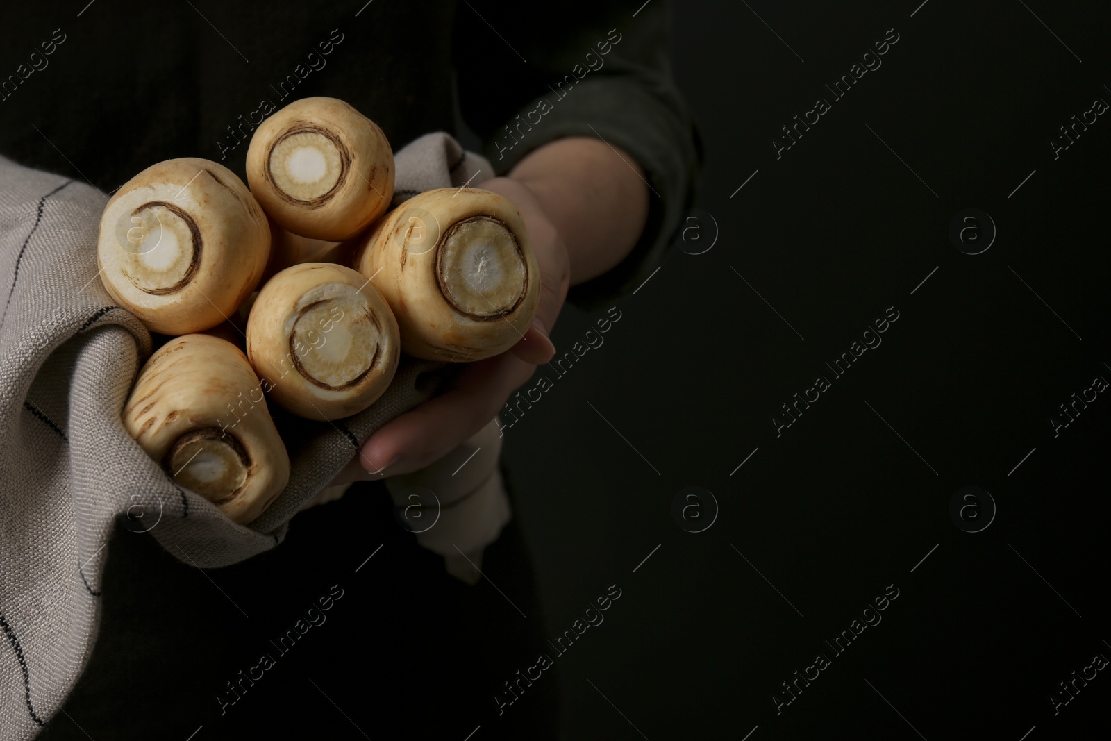 Photo of Woman holding fresh ripe parsnips on black background, closeup. Space for text