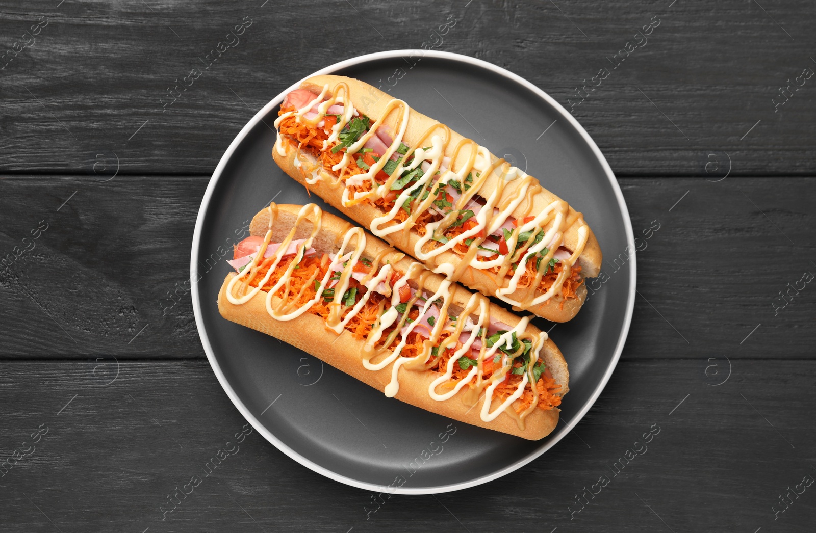 Photo of Delicious hot dogs with bacon, carrot and parsley on black wooden table, top view