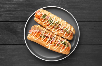 Delicious hot dogs with bacon, carrot and parsley on black wooden table, top view