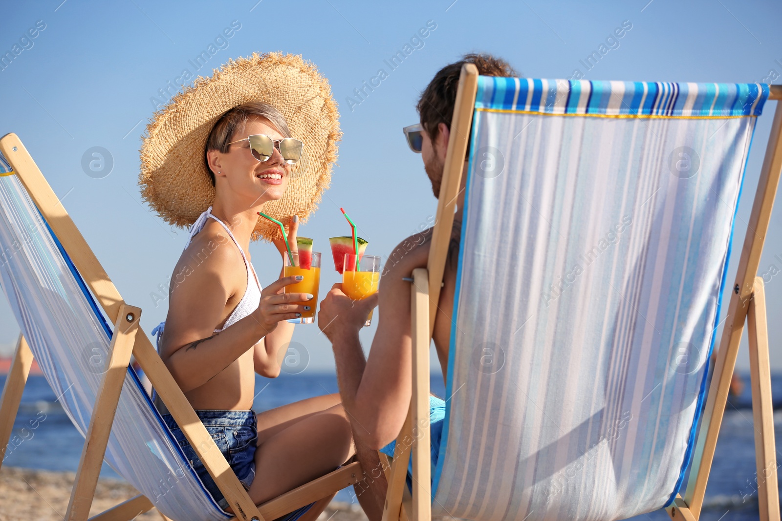 Photo of Young couple with cocktails in beach chairs at seacoast