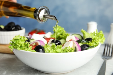 Photo of Dressing tasty fresh Greek salad with olive oil on grey marble table