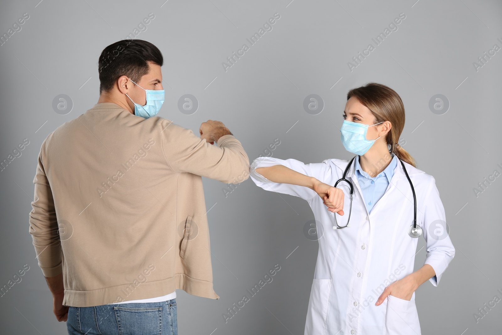 Photo of Doctor and patient doing elbow bump instead of handshake on light grey background. New greeting during COVID-19 pandemic